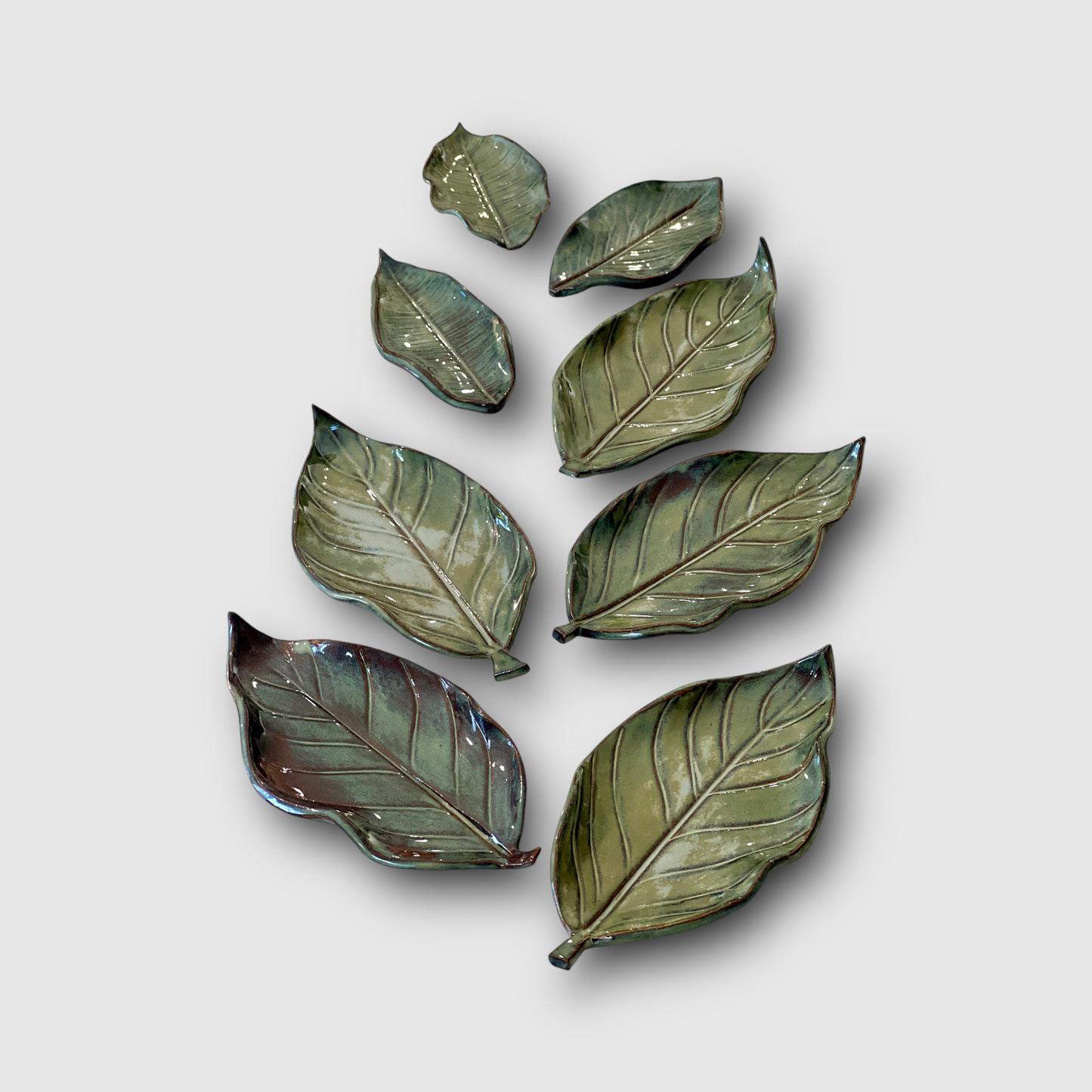 Collection of handmade ceramic leaf-shaped dishes in various sizes, featuring detailed vein patterns and natural green tones. A unique artisan gift, perfect for serving, jewelry storage, or as decorative nature-inspired home decor.