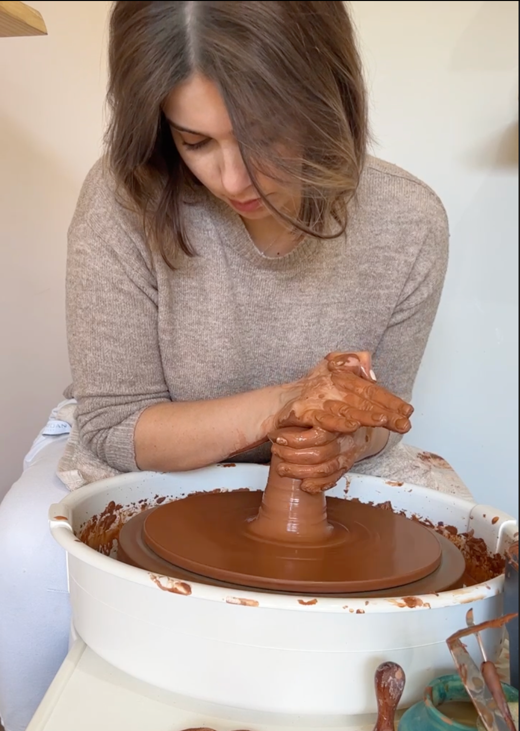 Potter shaping clay on a pottery wheel, hands covered in rich brown clay. Focused craftsmanship in a serene studio setting, capturing the art of handmade ceramics and wheelthrowing
